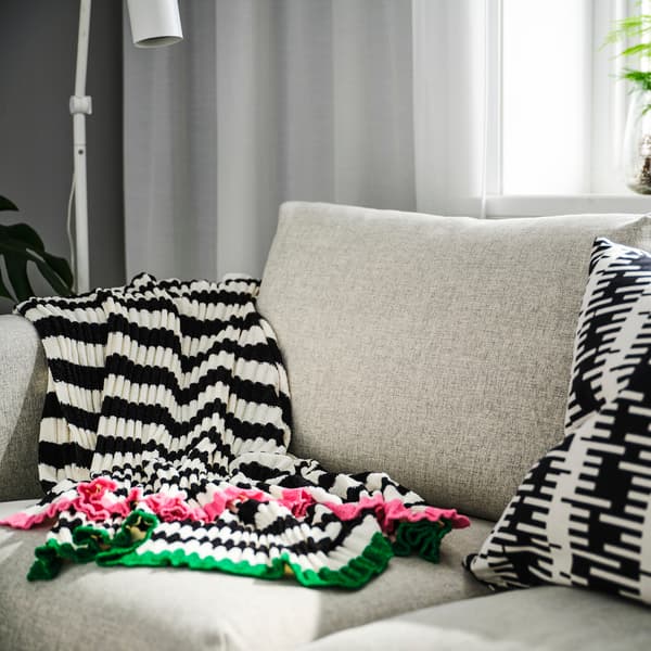LYs sofa med puder og en plaid i sort og hvide striber og lyserøde og grønne kanter.
