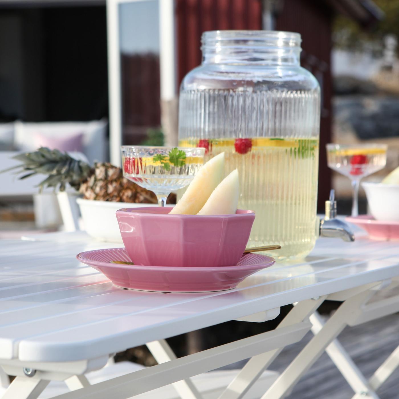Lyserødt service og en drikkedispenser med citronvand i står på et hvidt bord. 
