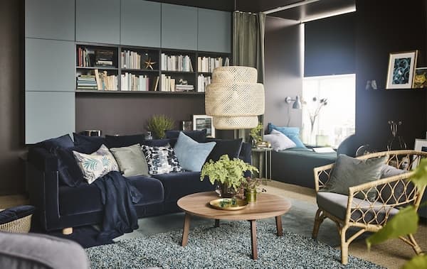 „Mach einfach alles hier“-Raum mit einem Sofa mit dunkelblauem Samtbezug, einem Couchtisch aus Nussbaumholz und einem Tagesbett mit einem grünen Vorhang.