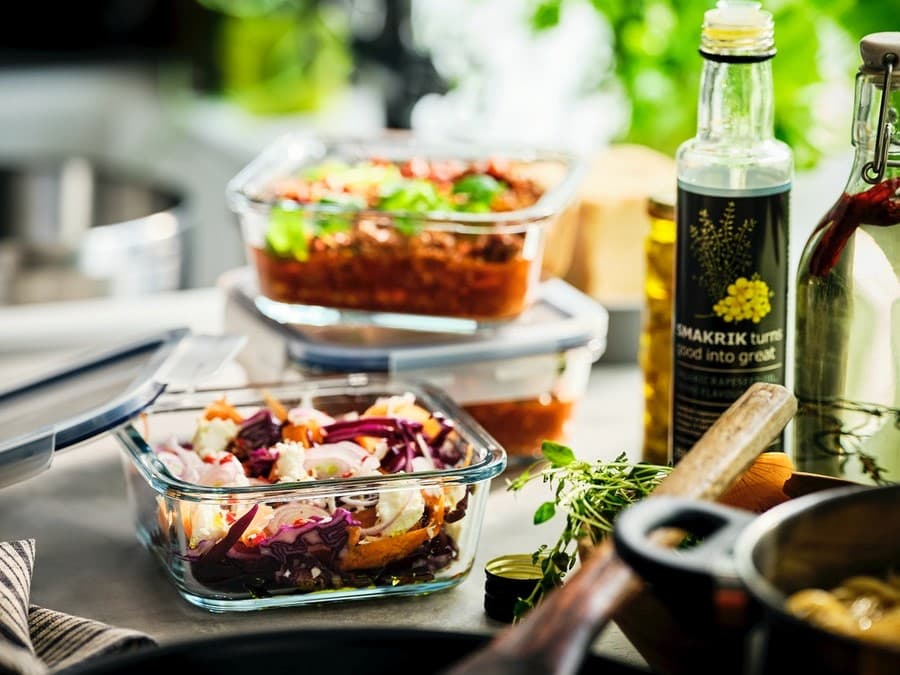 Madbeholdere af glas, som kan bruges til at opbevare madrester i, står på et køkkenbord med olier, en flaske vand og andet køkkengrej.