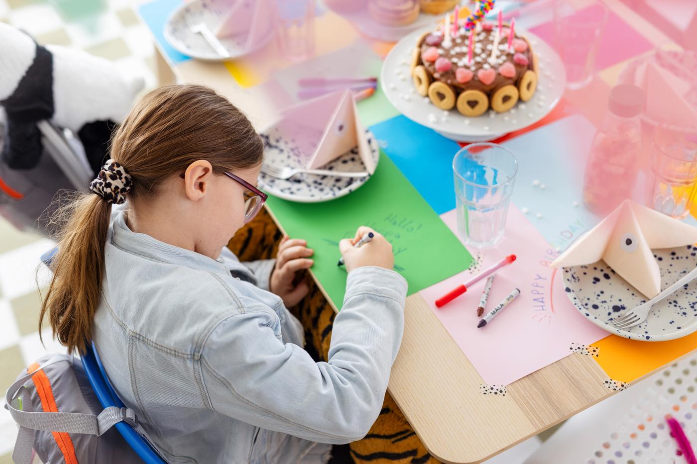 Mädchen malt auf Papier. Sie sitzt dabei am Geburtstagstisch 