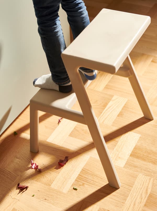 เด็กยืนอยู่บนบันไดขั้นล่างของเก้าอี้เตี้ย MÄSTERBY/แมสเตร์บี ที่วางถัดจากครัว เศษของหัวหอมแดงอยู่บนพื้น