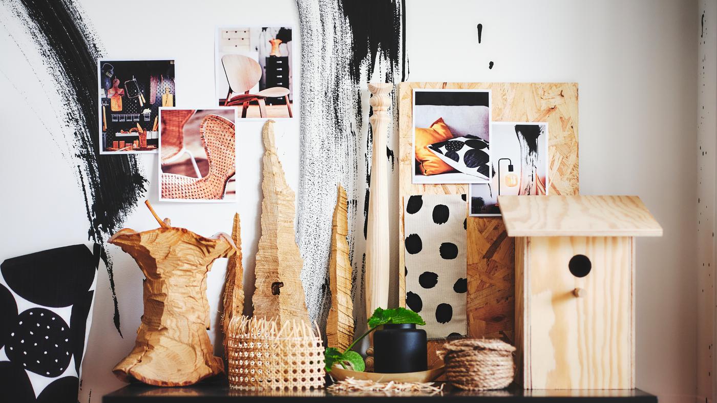 Mai multe obiecte, printre care și o vază KONSTFULL neagră, pe o suprafață plană în fața unor imagini lipite pe un perete.