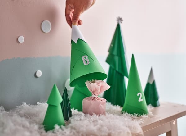 Main en train de soulever un sapin en papier faisant partie d'un calendrier de l'Avent en forme de forêt, révélant le petit cadeau qu'il cache.