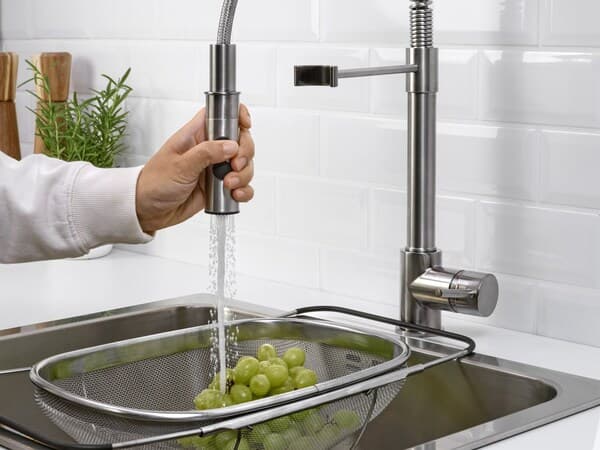 Main tenant un robinet d'où coule de l'eau directement sur des raisins placés dans une passoire sur un évier