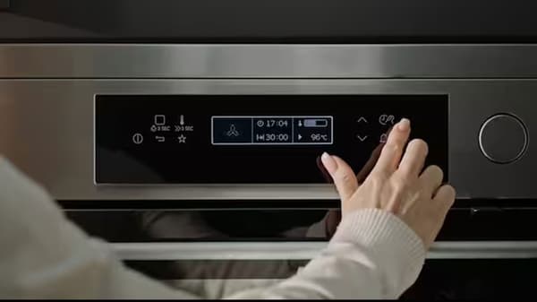 Main touchant une commande tactile sur un four en inox