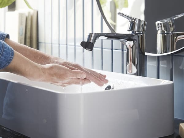Mains passées sous l'eau d'un robinet portant un embout.