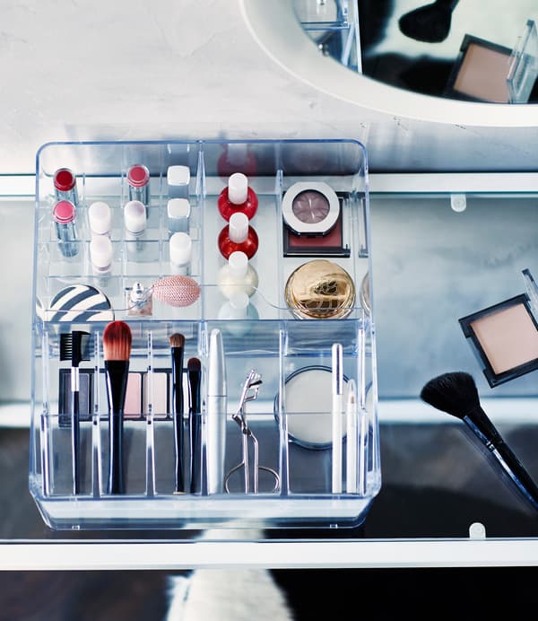 Make-up and make-up accessories organised in a clear IKEA GODMORGON box with compartments.