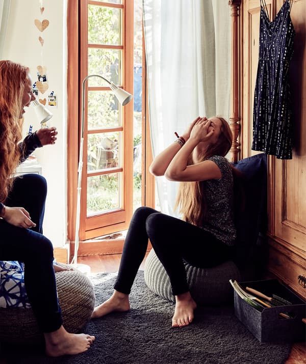Malin et Stine assises l’une en face de l’autre et occupées à rire à côté de portes-fenêtres.