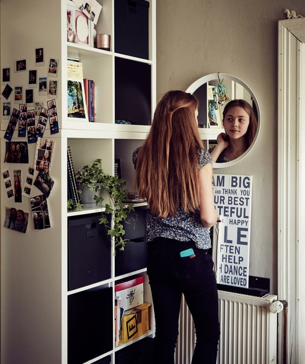 Malin occupée à se regarder dans le miroir à côté d’un cube de rangement.