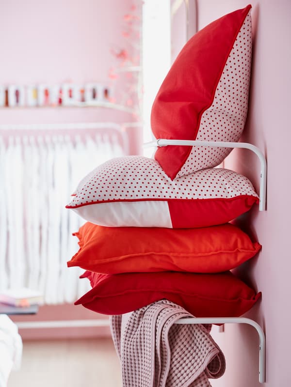 MALINMARIA red and white cushion covers stacked on wall mounted clothes bars.