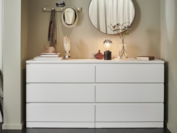 MALM chest of drawers in bedroom with a LINDBYN round mirror above it. A MOLNART light bulb on a MARKFROST base stands on top of the drawers and there are other decorative items placed neatly on top as well. 