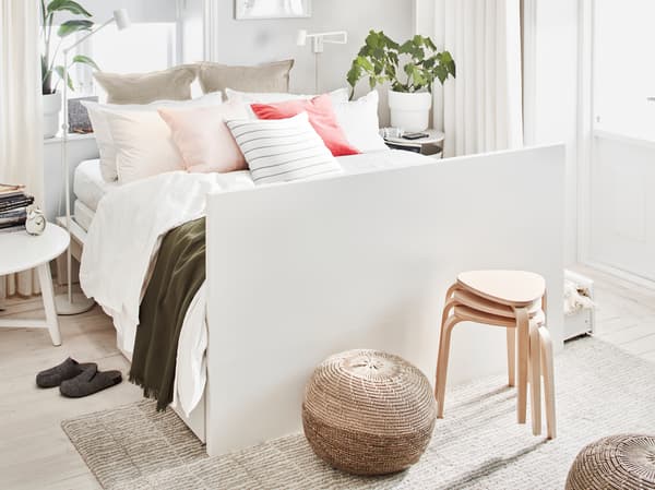เตียงคู่ MALM/มาล์ม สีขาว พร้อมหมอนและหมอนอิงหลายใบ และใช้หัวเตียงเป็นปลายเท้า ในห้องที่มีแสงสว่าง