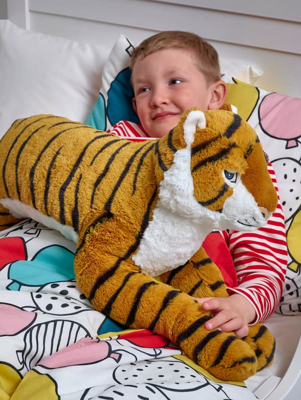 Malý chlapec leží v posteli, v náručí drží plyšového tigra DJUNGELSKOG.