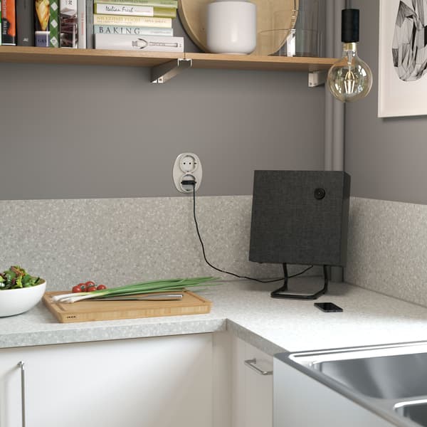 Mały, kwadratowy, czarny głośnik stereo Bluetooth® IKEA ENEBY, stojący na blacie w narożniku kuchni.