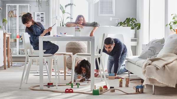 Maman et sa fille regardent papa et son autre fille jouer avec un ensemble de train sur le plancher du salon.