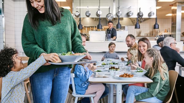 Maminka s dětmi sedí u stolu v restauraci IKEA, společně jedí udržitelné jídlo.
