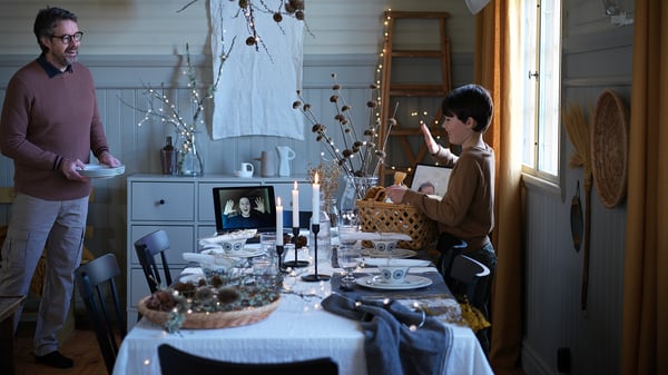 Man and boy setting a holiday table while speaking with man via video call.