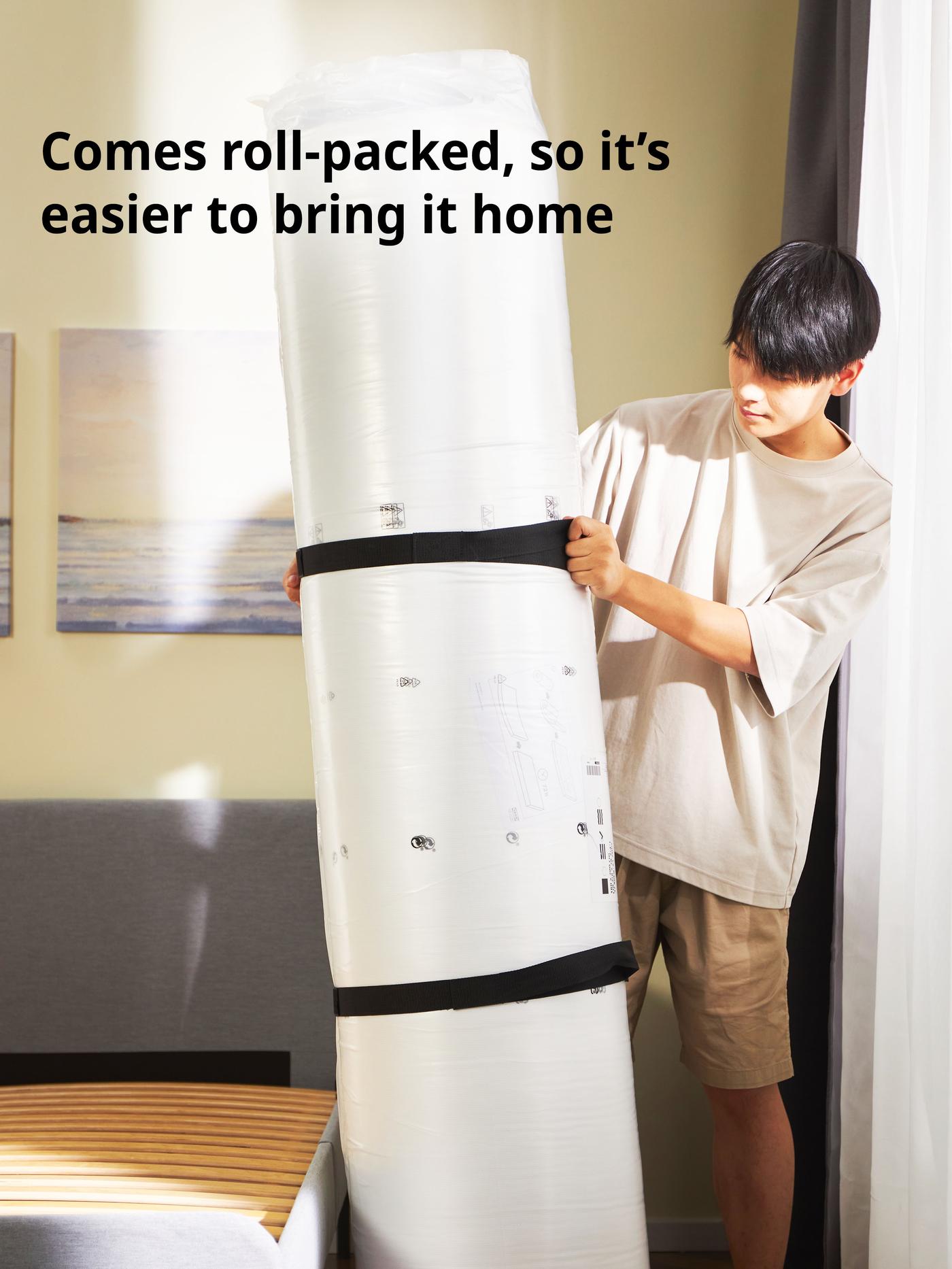 Man holding up a roll-packed VALEVÅG pocket sprung mattress, extra firm/light blue, 150x200 cm.