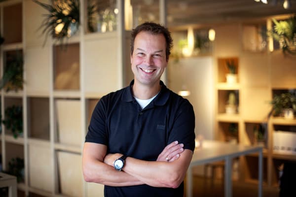 Man i svart pikétröja står med armar i kors och ler