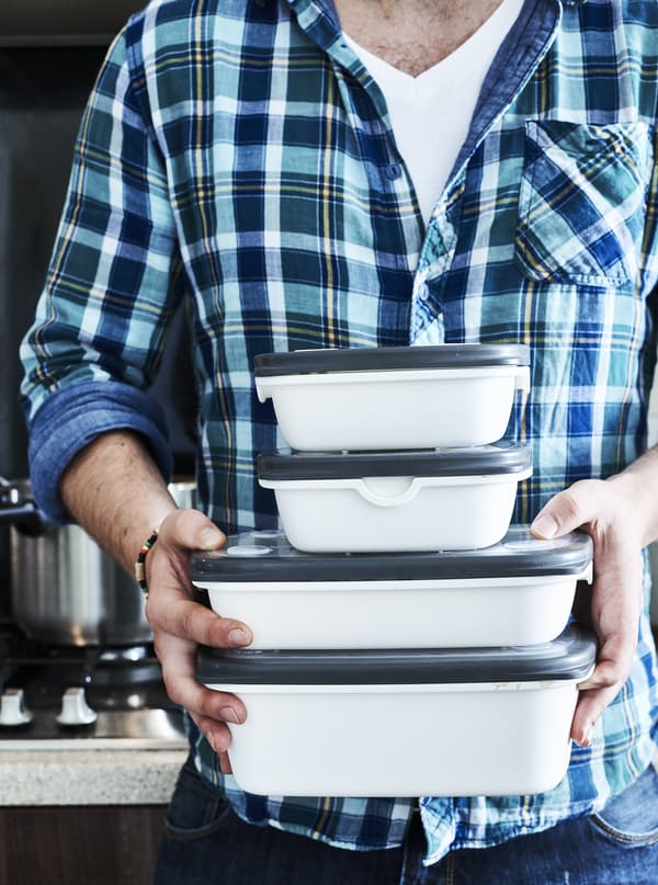 Man in blue shirt is holding four plastic containers stacked on top of each other.