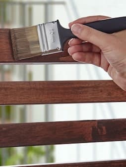 Man lakt houten meubel met kwast.