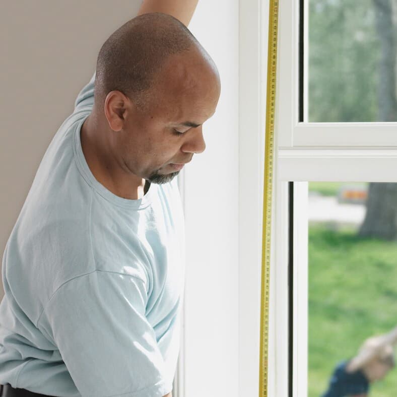 Man measuring a window in a home with a tape measure