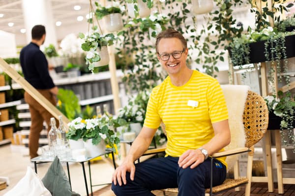 Man med glasögon och gul tröja sitter på en trästol och ler mot kameran