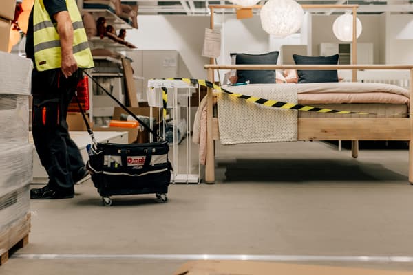Man med gul väst drar en svart vagn intill en säng i trä
