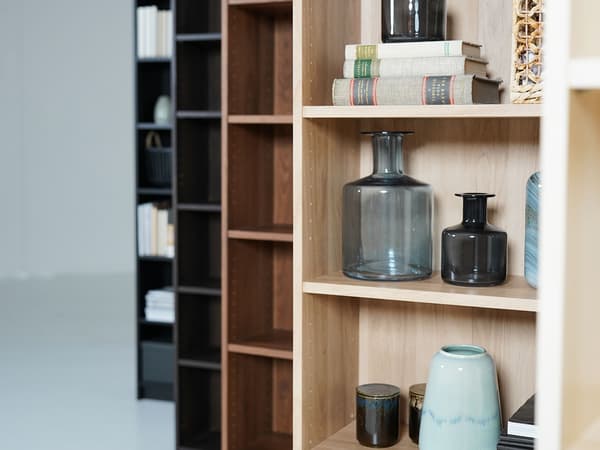 Man sieht ein offenes Regal, eine Vase und gestapelte Bücher.
