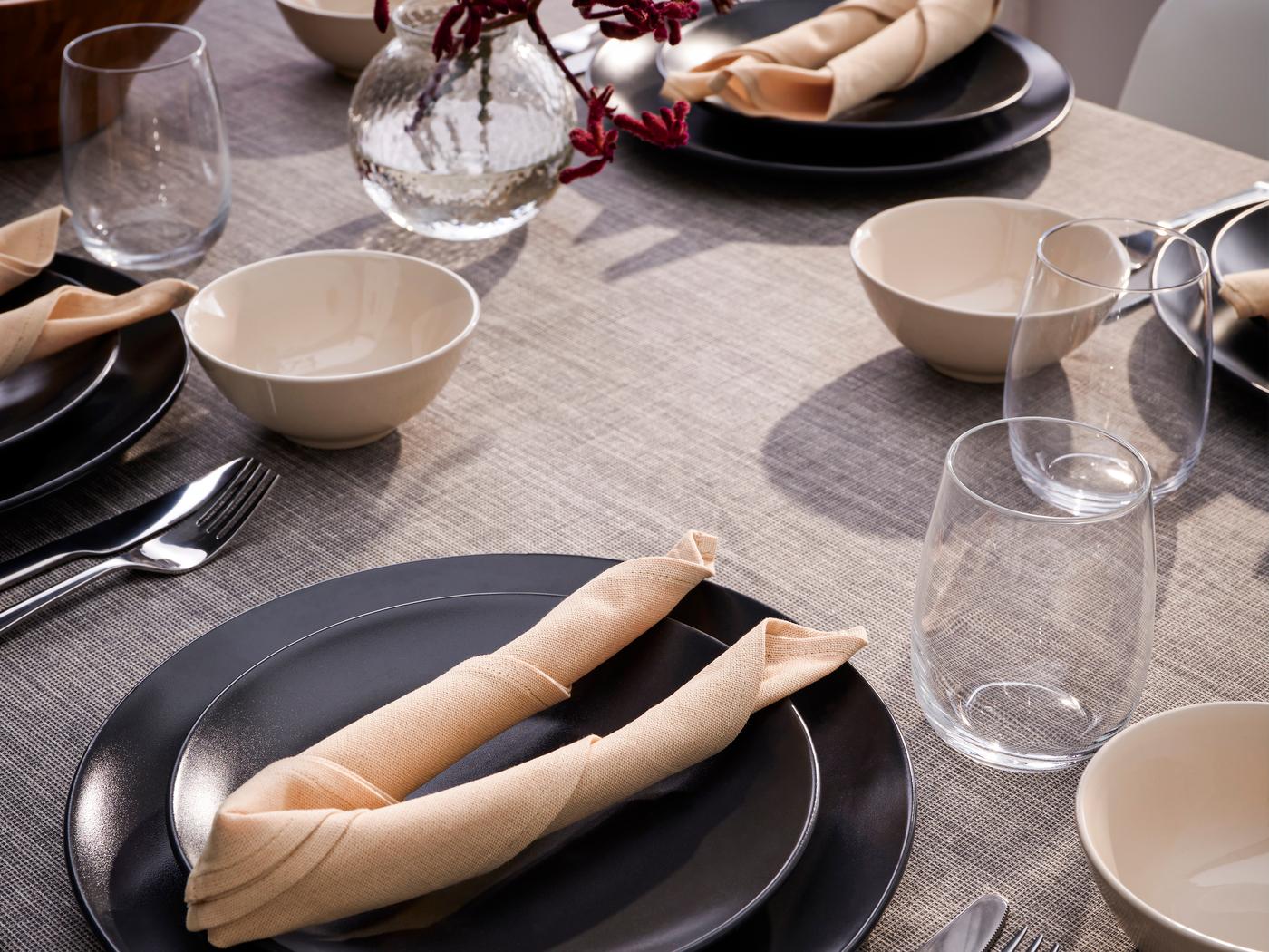 Man sieht eine gedeckte Tafel, schwarze Teller, Servietten, Gläser