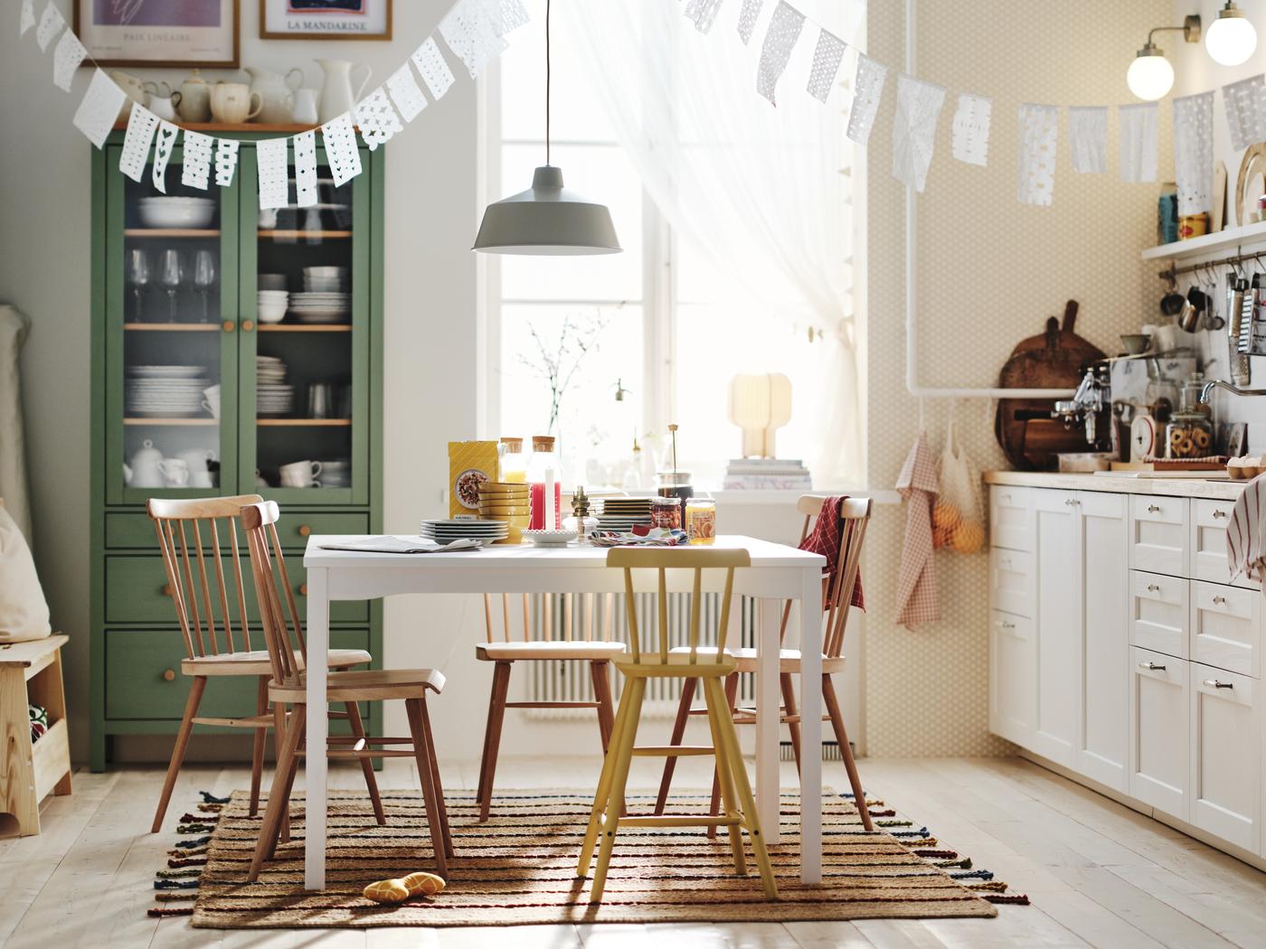 Man sieht eine weiße Küche, Esstisch, Stühle - eine helle, belebte Küche, freundlich. Dahinter eine grüne Vitrine. Es hängt eine Girlande