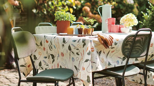 Man sieht einen Outdoor Tisch und zwei Stühle. Auf dem Tisch hat es einen Krug und einige Töpfe.