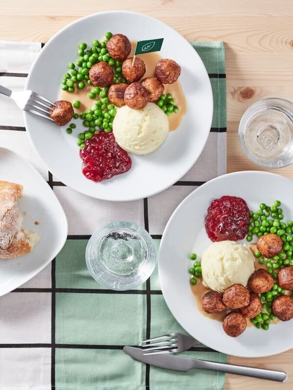 Man sieht mehrere Teller mit Fleischbällchen, Püree, Erbse und Preiselbeeren aus der Vogelperspektive auf einem Tisch stehen