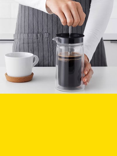 Man sieht wie jemand eine französische Kaffeepresse verwendet und darunter einen gelben Balken.