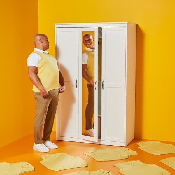 man trying on a sleeveless jumper in front of a wardrobe with a mirror