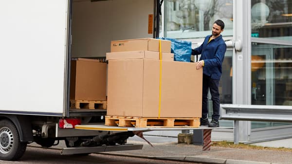 Man unloading a pallet of large boxes from a box truck.