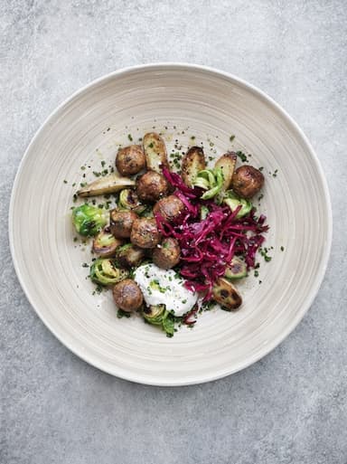 Mandonguilles vegetals amb cols de Brussel·les i col vermella en vinagre servides en un plat de fusta, vistes des de dalt.