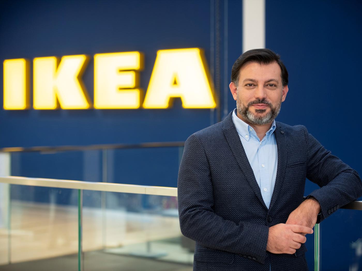 Mann in einem schwarz weißem Anzug steht lächeldn vor einem großen Ikea Neon Schild