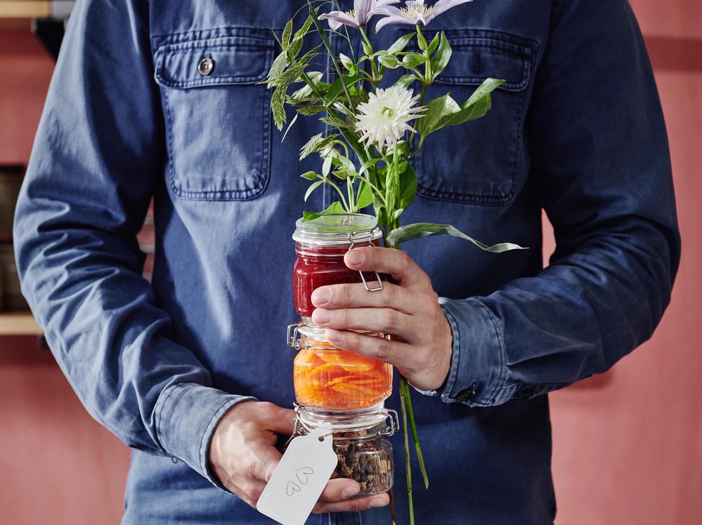 Mann in Jeanshemd hält ein Einmachglas voller eingelegtem Gemüse vor der Brust