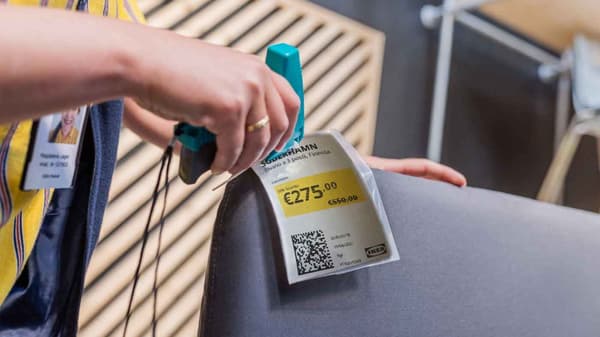 Mano di una co-worker IKEA che attacca il cartellino del prezzo su una poltrona grigia.