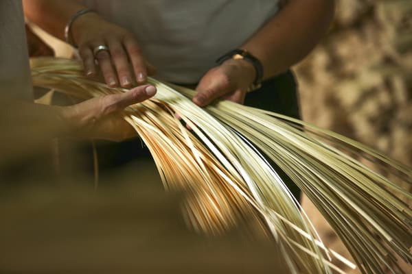 Manos armando una cesta de fibras naturales de colores verdes.
