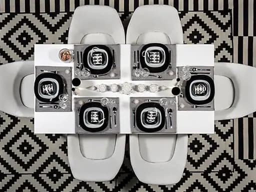 Mantel individual negro e branco con prato negro, outro prato fondo, unha cunca e xogo de cubertos de 24 pezas