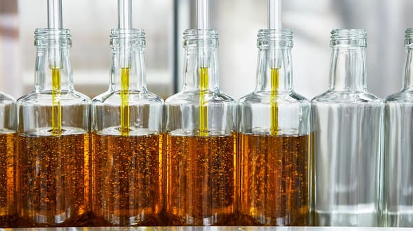 Many glass bottles standing side by side are being filled with organic, golden yellow IKEA SMAKRIK rapeseed oil.
