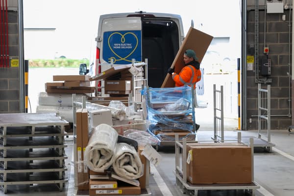 Many IKEA products in the front, waiting to be loaded. In the background a person loading a van with products.