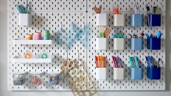 Many white pegboards with holes holding differently coloured containers storing colourful pens, paper clips and tape.