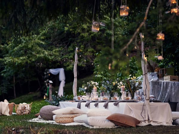 Mariage bohème en plein air dans un jardin avec des coussins sur le sol et des lanternes suspendues au-dessus d’une table.