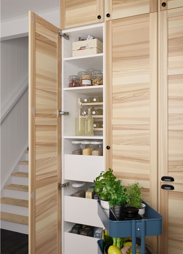 Massief essen IKEA TORHAMN kastdeuren met daarachter veel planken en lades, naast een donkerblauwe RÅSKOG roltafel.