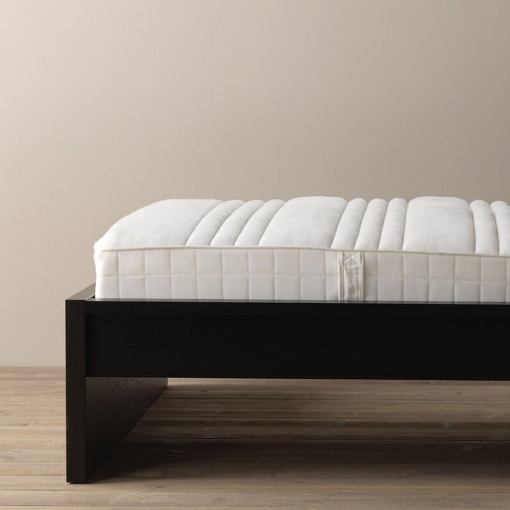 Matelas disposé dans un cadre de lit en bois noir.