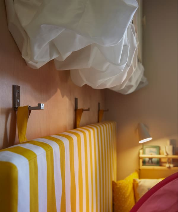 Matelas suspendu à des crochets muraux près d'un lit. Tissu blanc fixé sous des placards en volutes rappelant des nuages.
